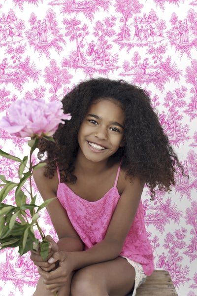 Mädchen vor einer Wand mit Toile-de-Jouy-Tapete und einer Pfingstrose in der Hand