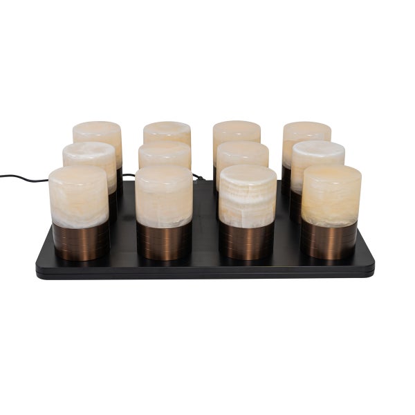 Zwölf zylindrische Tischlampen mit Schirmen in Steinoptik und Metallfuß auf einer schwarzen Ladestation.