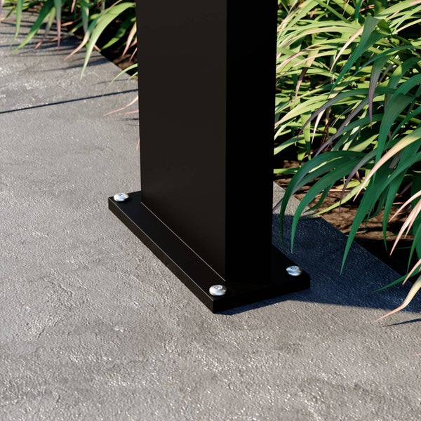 Nahaufnahme eines schwarzen Pfostenfußes aus Metall, der mit Schrauben auf einer grauen Steinfläche neben grünen Pflanzen befestigt ist.