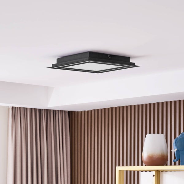 Quadratische LED-Deckenleuchte mit schwarzem Rahmen in einem modernen Wohnraum mit Holzlamellenwand.