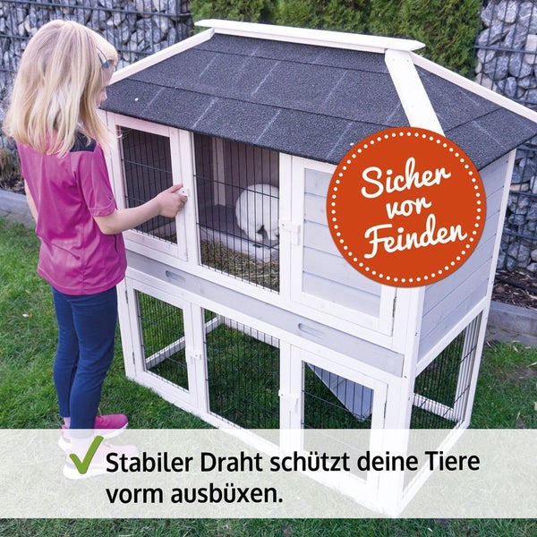 Zweistöckiger Kaninchenstall aus Holz mit wetterfestem Dach und stabilem Drahtgitter. Ein Kind steht neben dem Stall mit einem weißen Kaninchen.