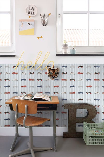 Kindertapete mit Oldtimer-Motiven auf gestreiftem Hintergrund in einem hellen Kinderzimmer mit Schreibtisch und Holzstuhl.
