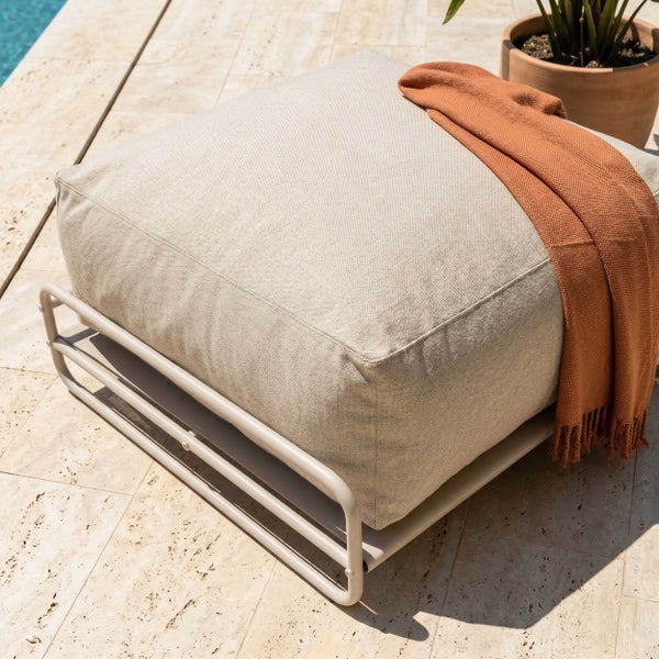 Gartenhocker mit Metallgestell und großem Textilpolster auf einer Steinterrasse neben einer Pflanze.
