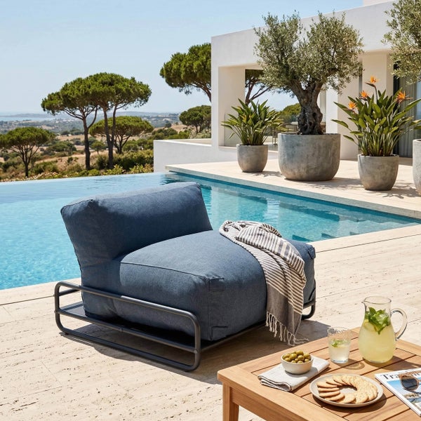 Moderne Outdoor-Lounge-Liege mit blauem Polster auf Metallgestell an einem Pool auf einer hellen Steinterrasse mit Pflanzen.