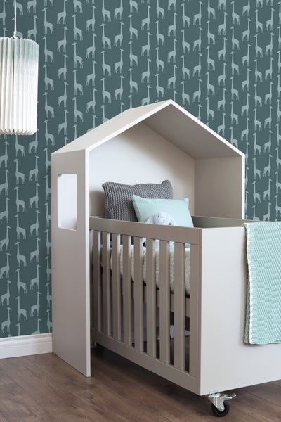 Kinderbett mit Hausrahmen, Textilien und Rollen vor einer Tapete mit Giraffenmuster