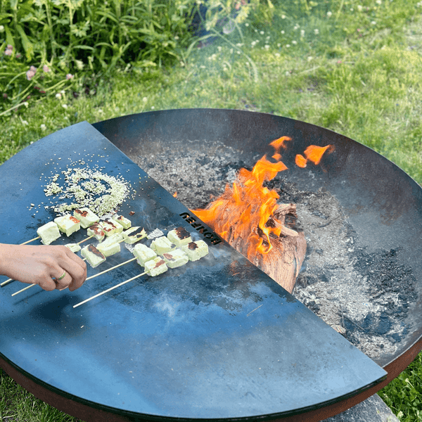 BonFeu Feuerschale mit einer Grillplatte aus Stahl, auf der Grillspieße über einem offenen Feuer zubereitet werden.