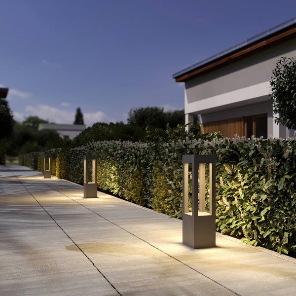 Moderne Wegeleuchten in Anthrazit beleuchten einen gepflasterten Gartenweg neben einer grünen Hecke bei Dämmerung.