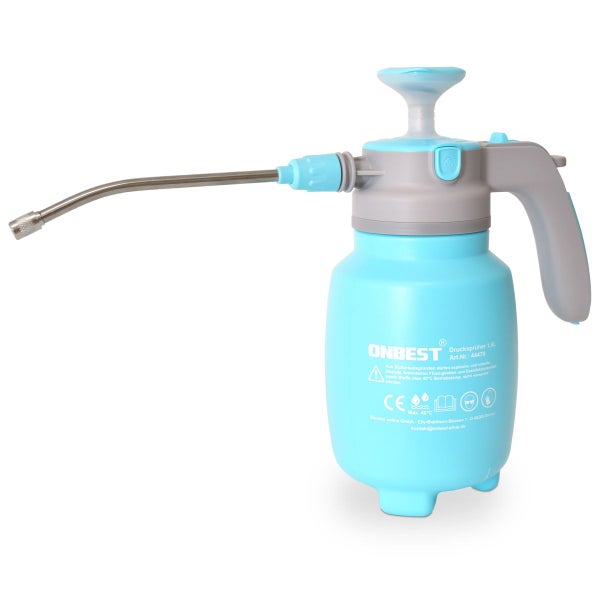 Eine Hand in einem grauen Handschuh sprüht mit einem blauen Drucksprüher Wassernebel auf eine grüne Zimmerpflanze auf einem Holztisch.