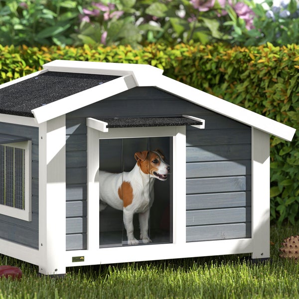 Moderne Hundehütte aus Holz mit Satteldach, weißem Rahmen und grauen Wänden, kleiner Hund im Inneren, auf einer Rasenfläche im Garten.
