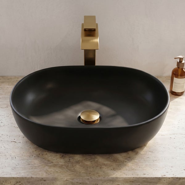 Ovale Aufsatzwaschschale in Schwarz mit goldfarbener Armatur und Ablaufventil auf einer hellen Steinplatte.