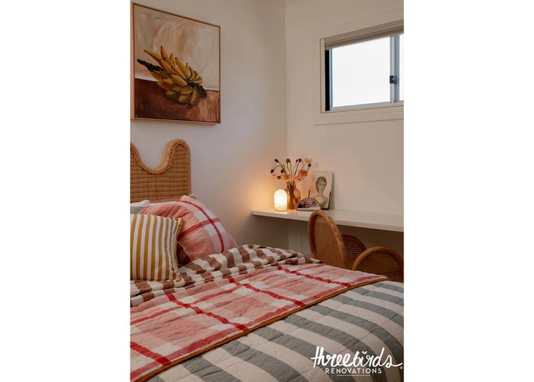 Gemütliches Schlafzimmer mit Rattan Kopfteil, karierter Bettwäsche, Schreibtisch mit Tischlampe und Wandbild in einem hellen, wohnlichen Ambiente.