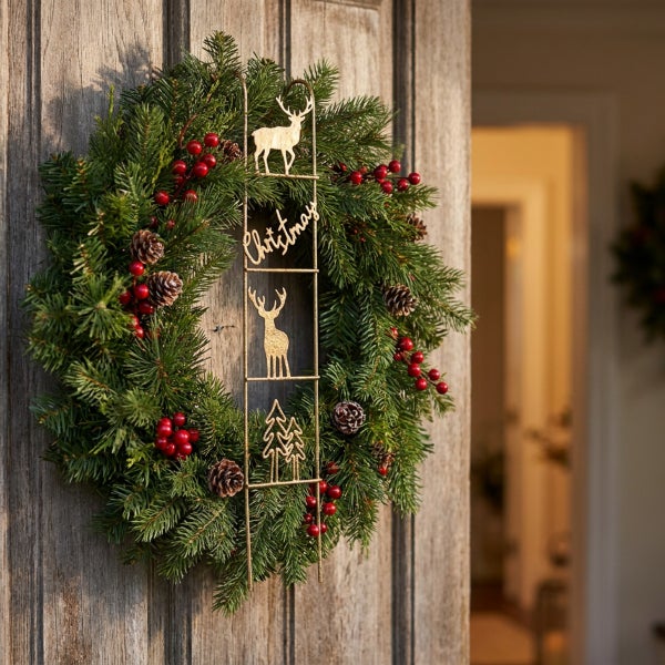 Weihnachtskranz aus Tannenzweigen mit roten Beeren Zapfen und einer hängenden Metallleiter mit Rentier und Weihnachtsbaum Motiven an einer Tür