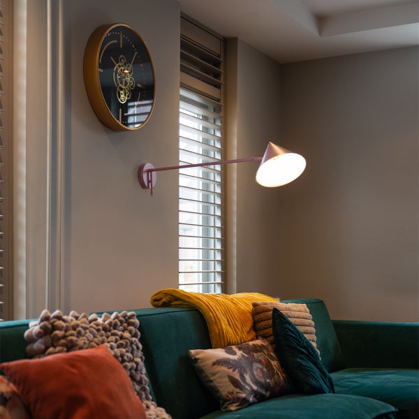 Wohnzimmer mit Sofa, Kissen, Tagesdecke, Wanduhr und Wandleuchte