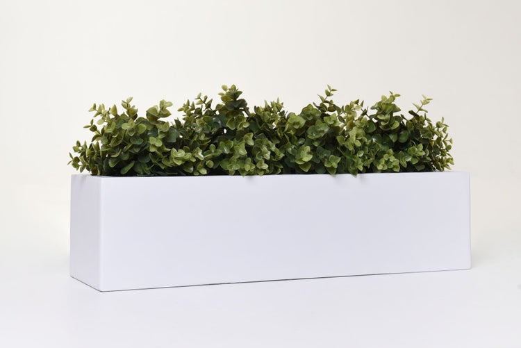 Künstliche Pflanze in einem rechteckigen weißen Blumenkasten.