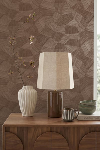 Braune Tapete mit geometrischem Polygonmuster hinter einer Holzkommode mit einer Tischlampe und einer Vase mit einem blühenden Zweig.