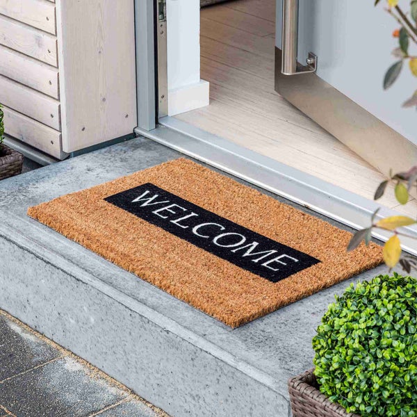 Fußmatte aus Kokosfaser mit Willkommensaufschrift vor einer offenen Tür
