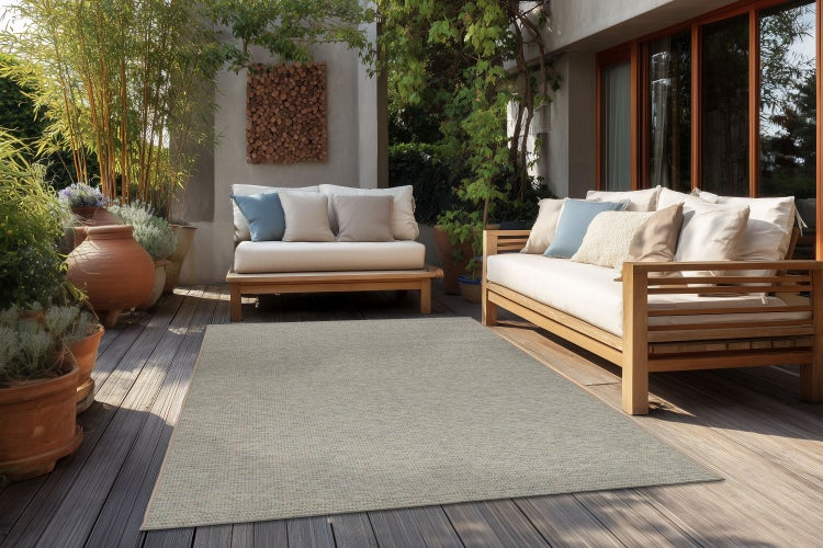 Rechteckiger Outdoor-Teppich auf einer Holzterrasse mit Sitzmöbeln aus Holz und Pflanzen in Terrakottatöpfen.