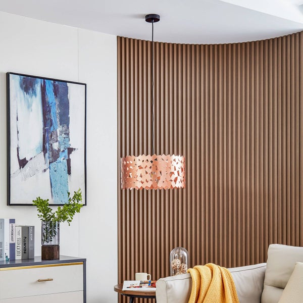 Moderne Hängeleuchte in Kupferfarben mit geometrischem Lochmuster in einem Wohnzimmer mit Akustikpaneelen aus Holz und abstrakter Wandkunst.