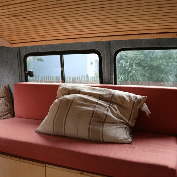 Innenraum eines Wohnmobils mit Holzdecke, Fenstern und Kissen auf einem Sofa.