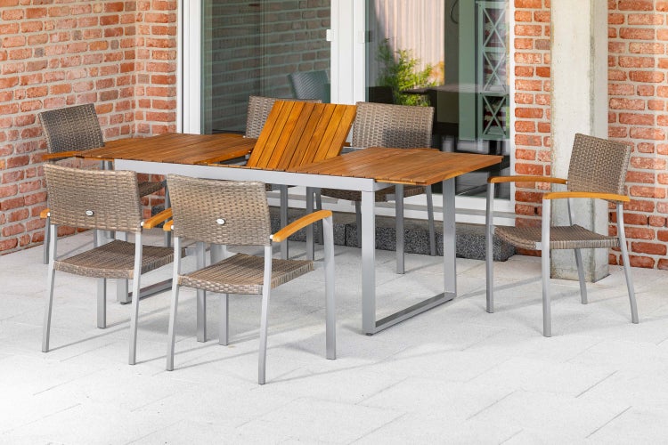 Gartenmöbel-Set mit ausziehbarem Tisch aus Holz und Aluminium sowie sechs Sesseln mit Geflecht auf einer gepflasterten Terrasse.