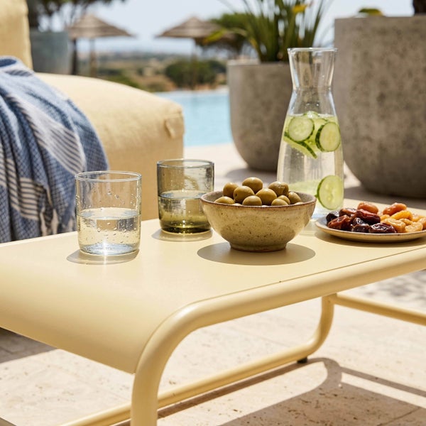 Moderner Metall-Beistelltisch für den Außenbereich mit Karaffe, Gläsern, Oliven und Trockenfrüchten auf einer sonnigen Terrasse am Pool.