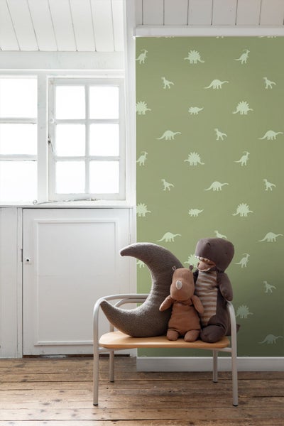 Kinderzimmer mit Dinosaurier-Tapete, Halbmondkissen und Stofftieren auf einem Stuhl