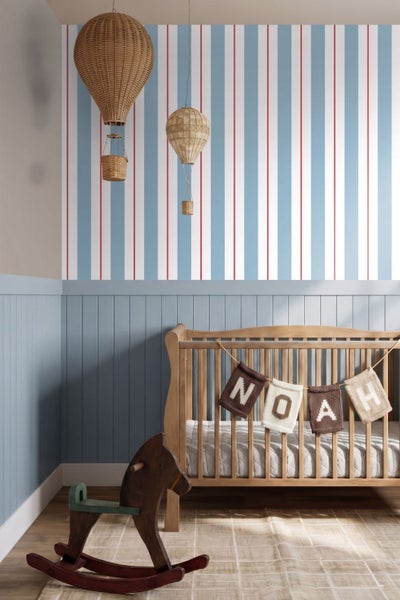 Helles Kinderzimmer mit Babybett aus Holz, Schaukelpferd, gestreifter Tapete, blauen Wandpaneelen und Deko-Heißluftballons aus Korbgeflecht.