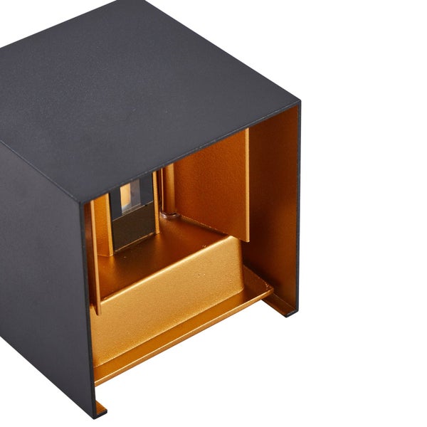 Würfelförmige Wandleuchte mit matt schwarzer Außenseite und goldener Innenseite sowie verstellbaren Klappen zur Steuerung des Lichtkegels.