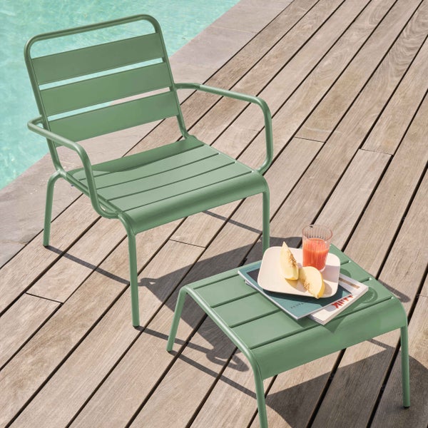 Grüner Garten-Sessel und Beistelltisch aus Metall mit Lamellen-Design auf einer hellen Holzterrasse direkt an einem Pool.