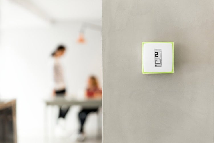 Digitales Wandthermostat mit LCD-Anzeige der Temperatur, montiert an einer Wand in einem hellen Wohnraum.