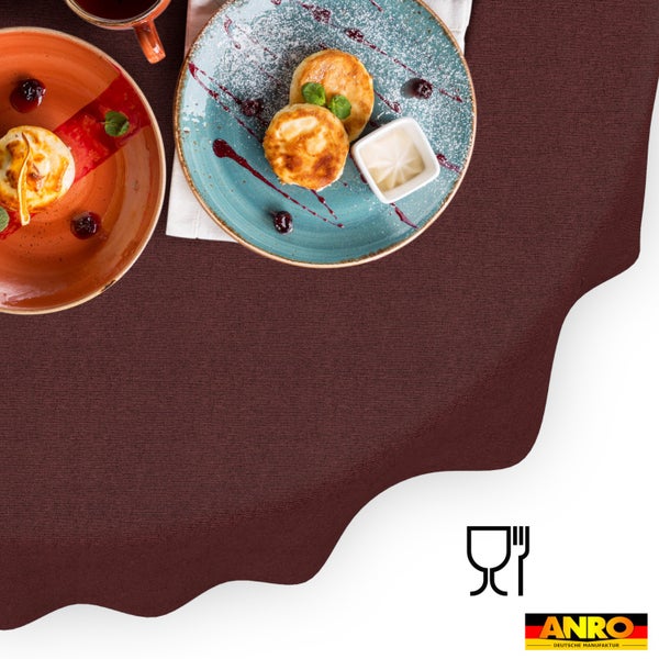 Strukturierte Tischdecke mit Symbol für Lebensmittelechtheit und ANRO Deutsche Manufaktur Logo auf einem gedeckten Tisch mit Tellern.
