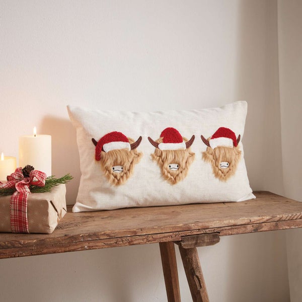 Dekokissen mit schottischen Hochlandrindern mit Weihnachtsmützen auf einem Holztisch