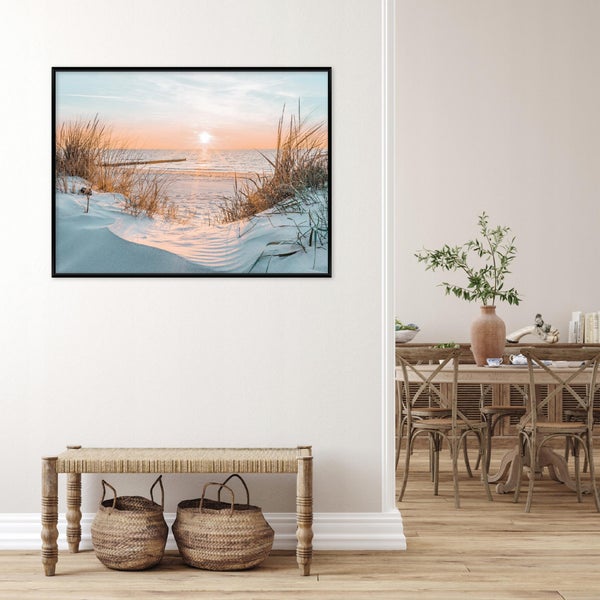 Wandbild mit Strandmotiv in schwarzem Rahmen ueber einer Sitzbank mit geflochtenen Koerben in einem hellen, natuerlich eingerichteten Wohnraum.