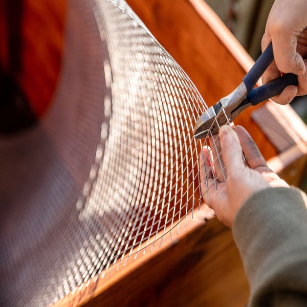 Eine Person schneidet Drahtgeflecht mit einer Zange an einem Holzkasten.
