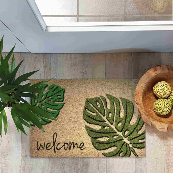 Fußmatte mit Monstera Blätter Muster und Willkommensgruß vor einer Tür.