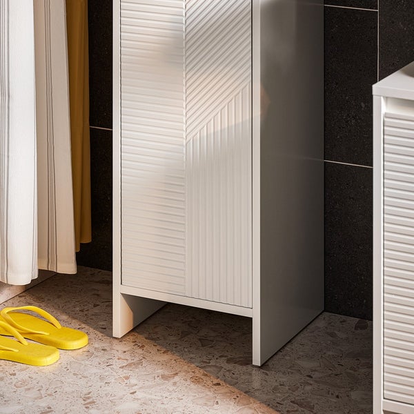 Detailansicht eines weißen Badezimmerschranks mit strukturierter Tür und gelben Badeschuhen auf dem Boden