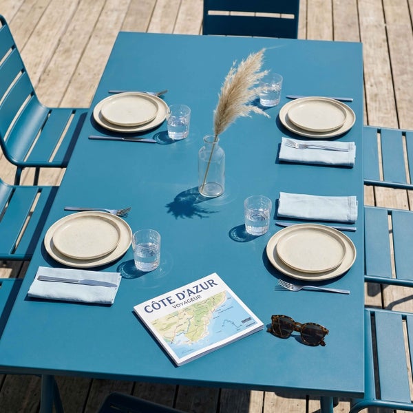 Moderner blauer Gartentisch aus Metall mit passenden Gartenstühlen, gedeckt für vier Personen auf einer Holzterrasse.
