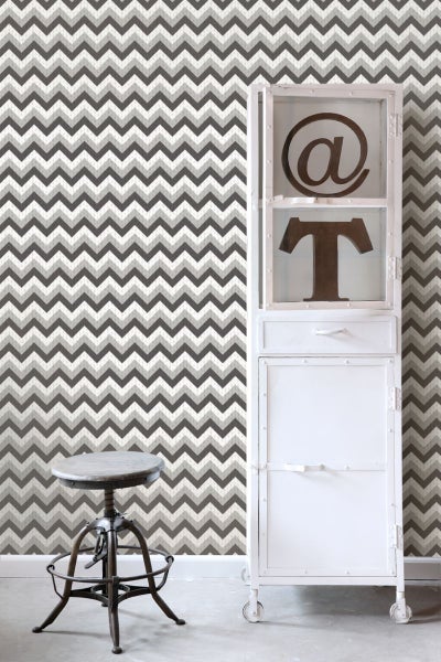 Tapete mit Zickzackmuster im Wohnraum, kombiniert mit einem Schrank und einem Hocker