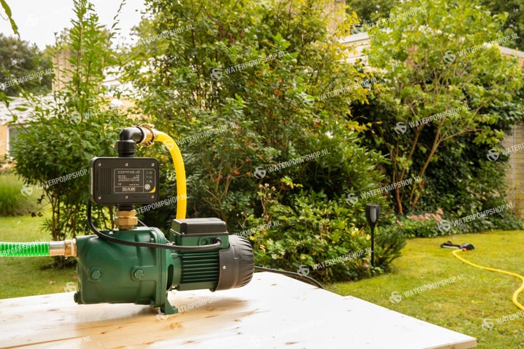 Garten mit Hauswasserwerk, gelbem Schlauch und grüner Pumpe auf Holztisch