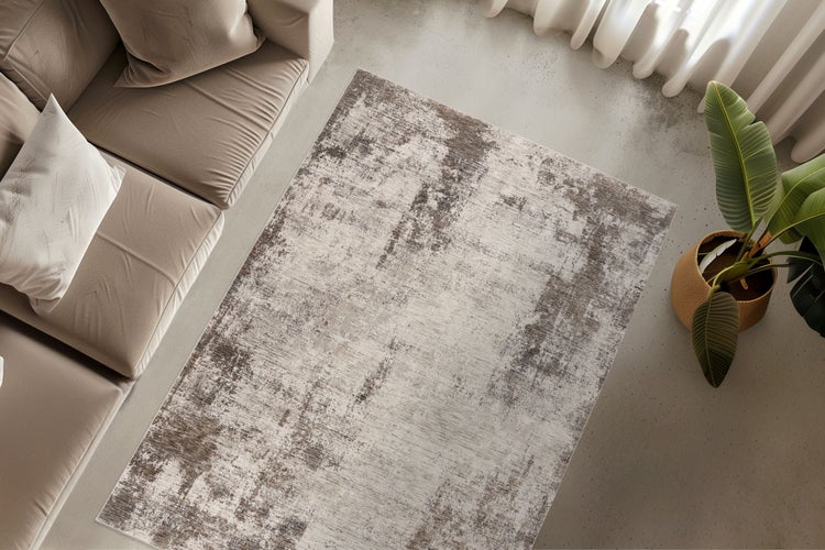 Wohnzimmer mit modernem, rechteckigem Teppich mit abstraktem Vintage-Muster, platziert vor einem Sofa auf einem Betonboden mit einer Zimmerpflanze.