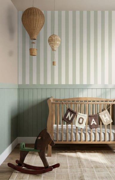 Kinderzimmer mit Wandvertäfelung und gestreifter Tapete. Ein Babybett aus Holz, ein Schaukelpferd und geflochtene Heißluftballons dekorieren den Raum.