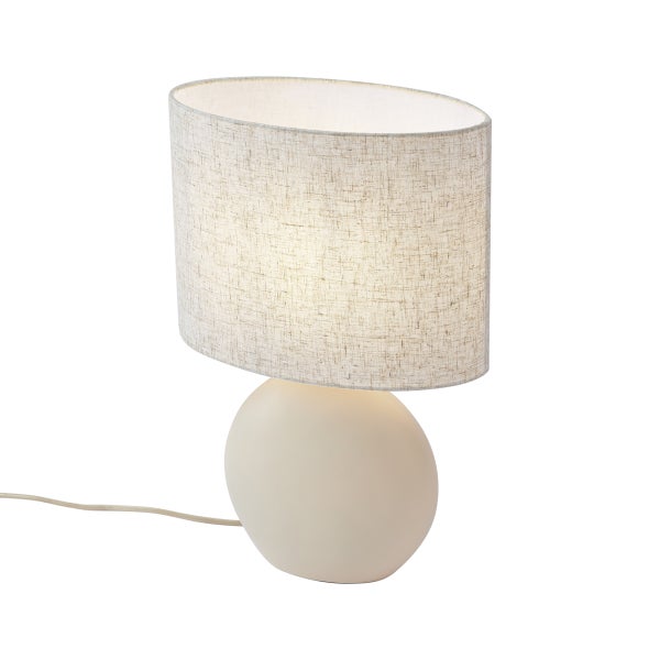 Tischleuchte mit beigem ovalem Textilschirm und rundem Lampenfuß, eingeschaltet.