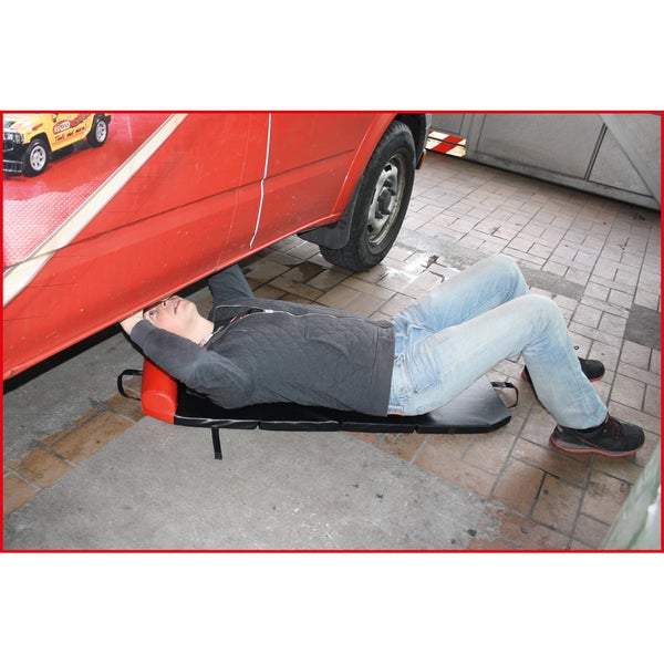 Eine Person liegt auf einer Montageliege unter einem Fahrzeug.