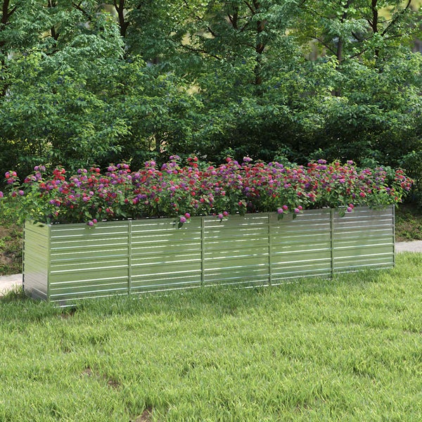 Großes rechteckiges Hochbeet aus verzinktem Metall, bepflanzt mit bunten Blumen, auf einer Rasenfläche vor grünen Sträuchern.