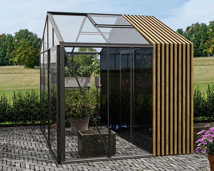 Modernes, helles Gewächshaus mit Glaswänden, dunklem Metallrahmen und Holzlamellen auf einer gepflasterten Terrasse in einem Garten.