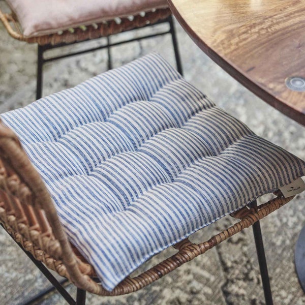 Gestreiftes Stuhlkissen von Tom Tailor auf einem Rattanstuhl neben einem Holztisch.