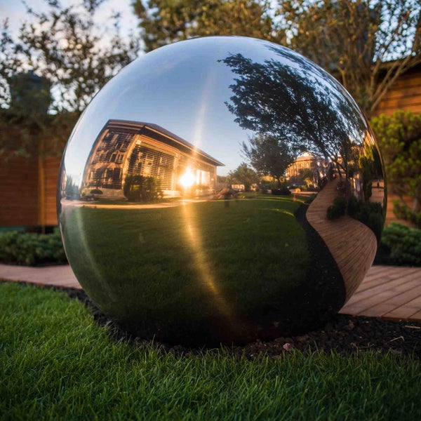 Große spiegelnde Gartenkugel aus Edelstahl auf einer Rasenfläche.