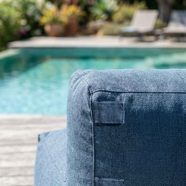 Blaues Outdoor-Kissen mit strukturierter Oberfläche und Befestigungslasche vor einem Swimmingpool.