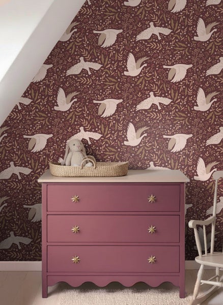 Mustertapete mit fliegenden Vögeln und floralen Motiven in einem Zimmer mit rosa Kommode und Stoffhase in einem Weidenkorb.