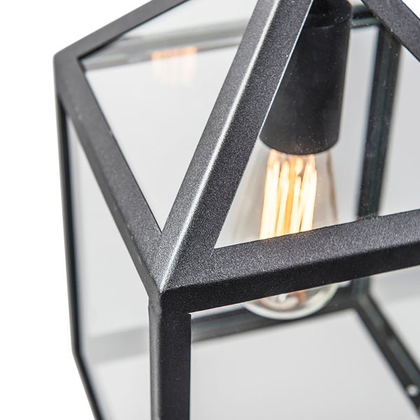 Nahaufnahme einer schwarzen Metalllaterne mit Glaseinsätzen und einem dekorativen Filament-Leuchtmittel im Inneren.